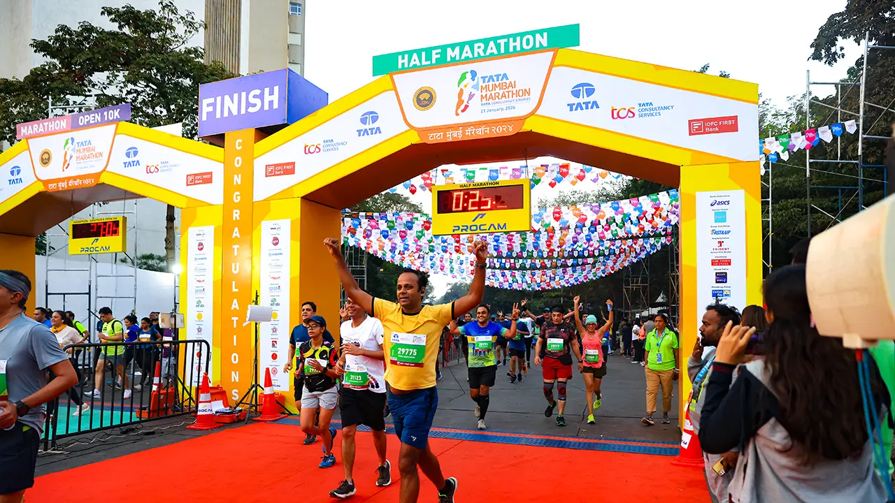 Finish gate at Tata Mumbai Marathon Half Marathon 2024, with jubilant runners celebrating under vibrant paper flags and Procam timing clocks