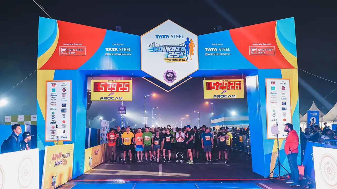 Early morning start line at Tata Steel Kolkata 25K 2023, featuring bold sponsor branding, twin Procam digital clocks, and runners poised for the elite 25K flag-off