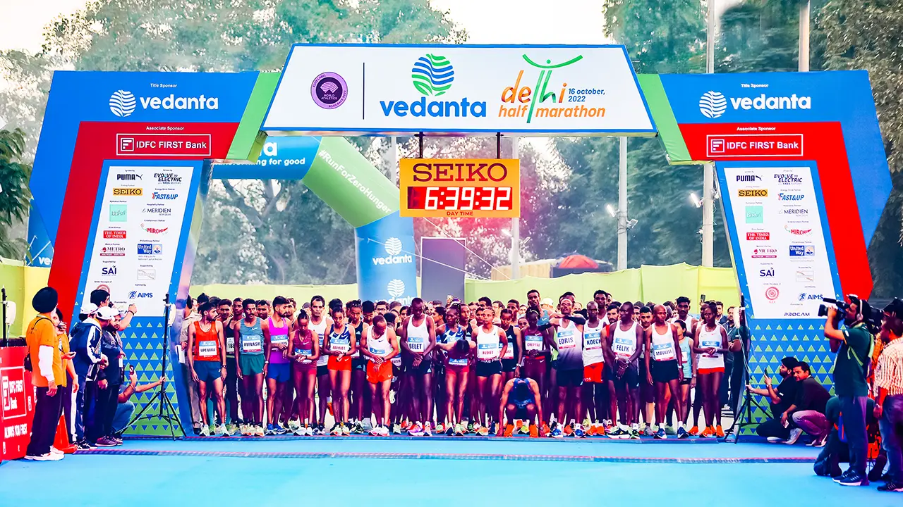 Elite athletes at the starting line of the Vedanta Delhi Half Marathon 2022 under a branded SEIKO-timed gate, showcasing sponsor visibility and international participation