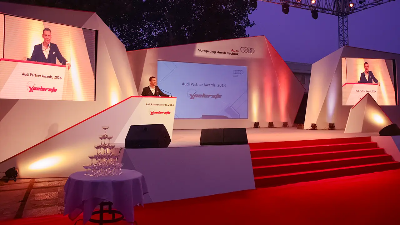 Audi Partner Awards 2014 — polygonal, geometric, asymmetrical stage design echoing Audi’s progressive design language, with sharp architectural angles, immersive lighting, and twin projection screens