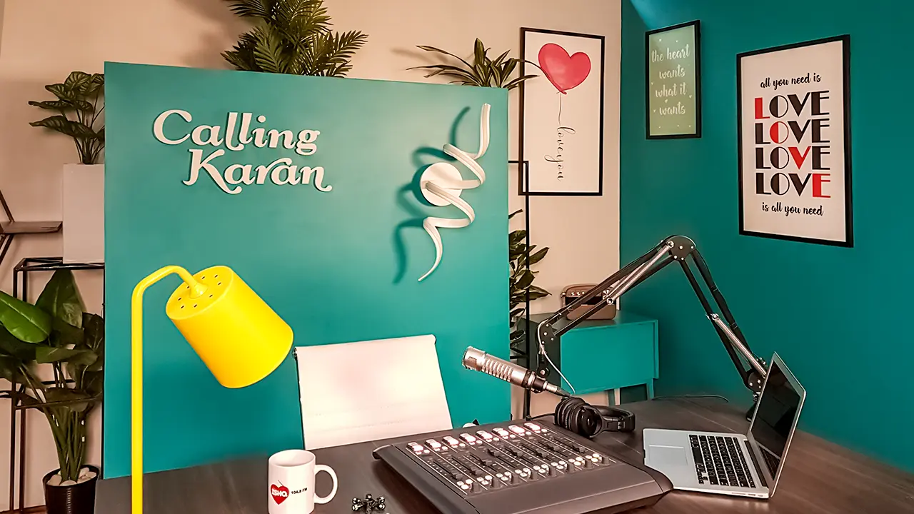 Calling Karan Season 2 set close-up with teal panel, yellow lamp, mic, control console and romantic wall art.