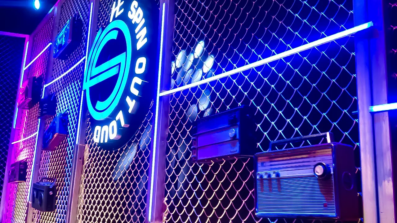 Close-up of HE Spin Out Loud stage mesh wall with vintage radios and neon lighting for retro-themed webisode series
