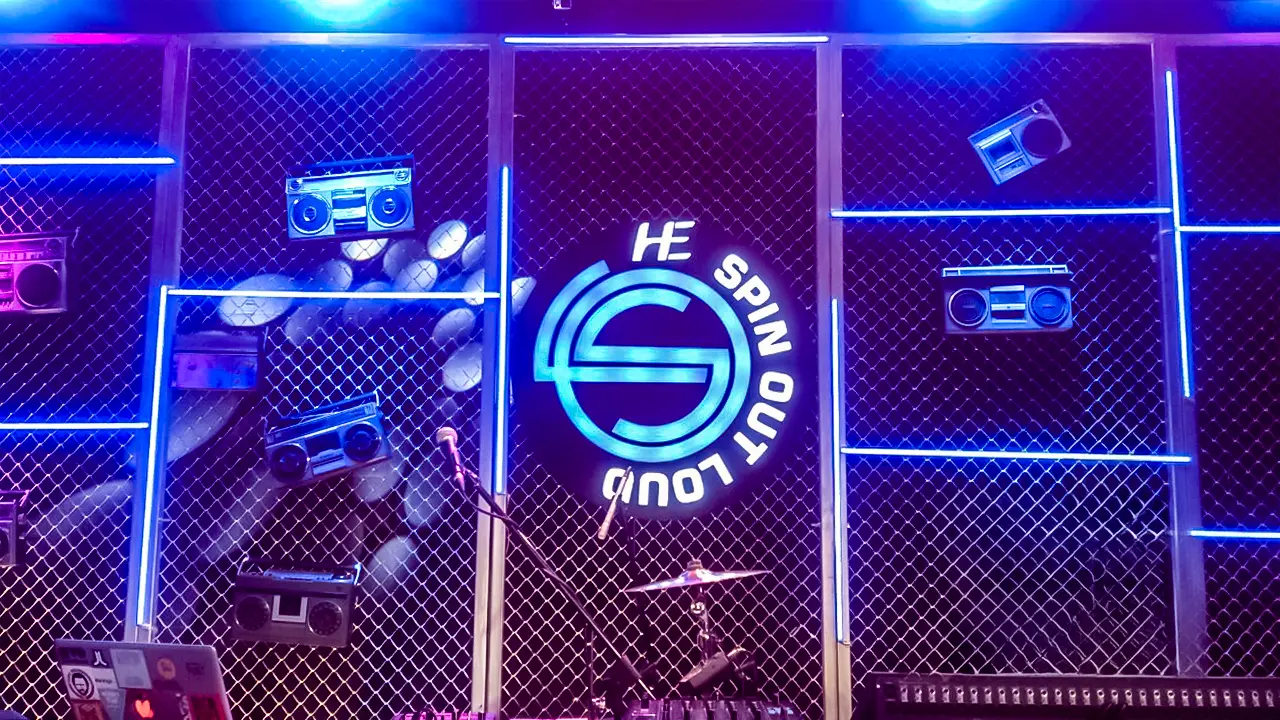 Stage backdrop for HE Spin Out Loud featuring retro boomboxes and neon grid design for youth-focused webisode series