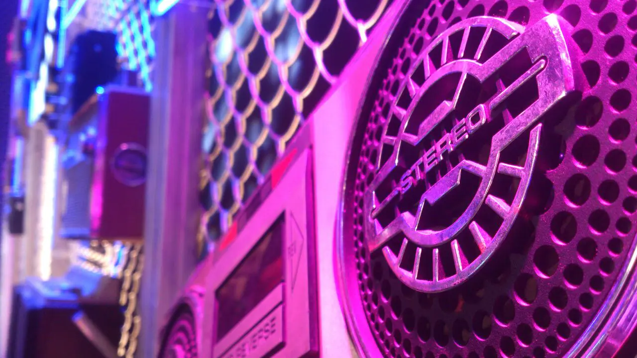 Close-up of HE Spin Out Loud boom box with retro stereo grille detailing and neon purple-blue event lighting